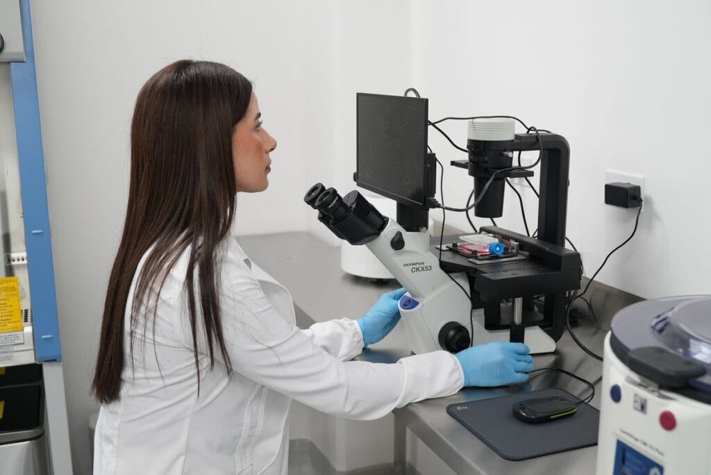Blast Institute scientist examining reprogrammed cell cultures under an inverted microscope in the lab