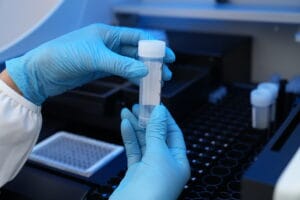 Researcher in blue gloves holding a sample tube at a laboratory analyzer